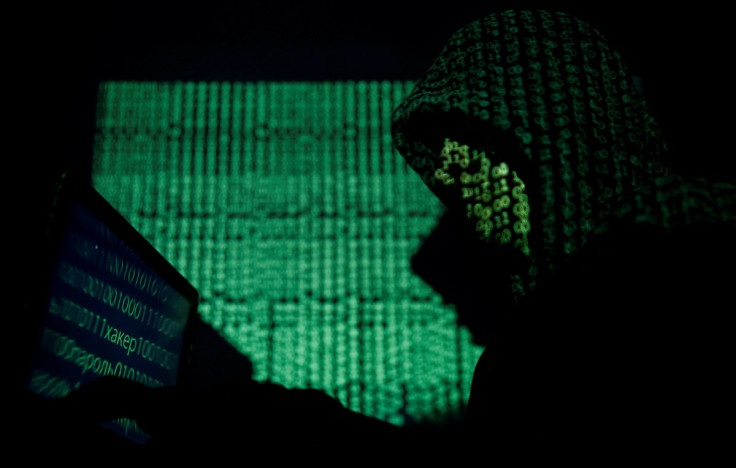 L&#39;uomo incappucciato tiene in mano un computer portatile mentre il codice informatico viene proiettato su di lui in questa immagine illustrativa