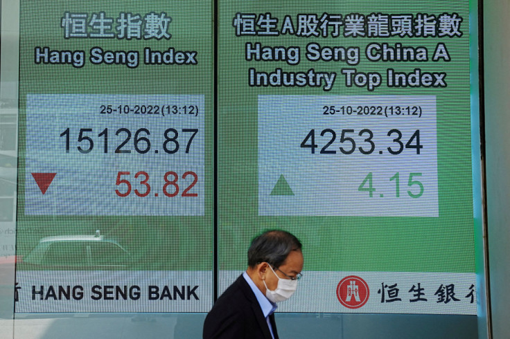 Una persona passa davanti a uno schermo che mostra l'indice azionario Hang Seng nel distretto centrale, a Hong Kong