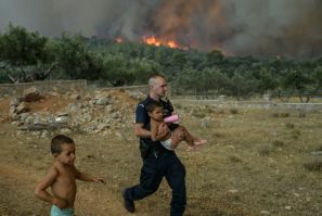 Un agente di polizia greco evacua un bambino da un incendio nel villaggio di Agios Charamlabos, vicino ad Atene